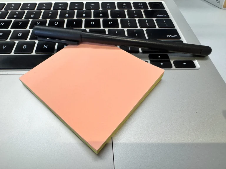 Black pen and peach sticky notes resting on a silver laptop keyboard