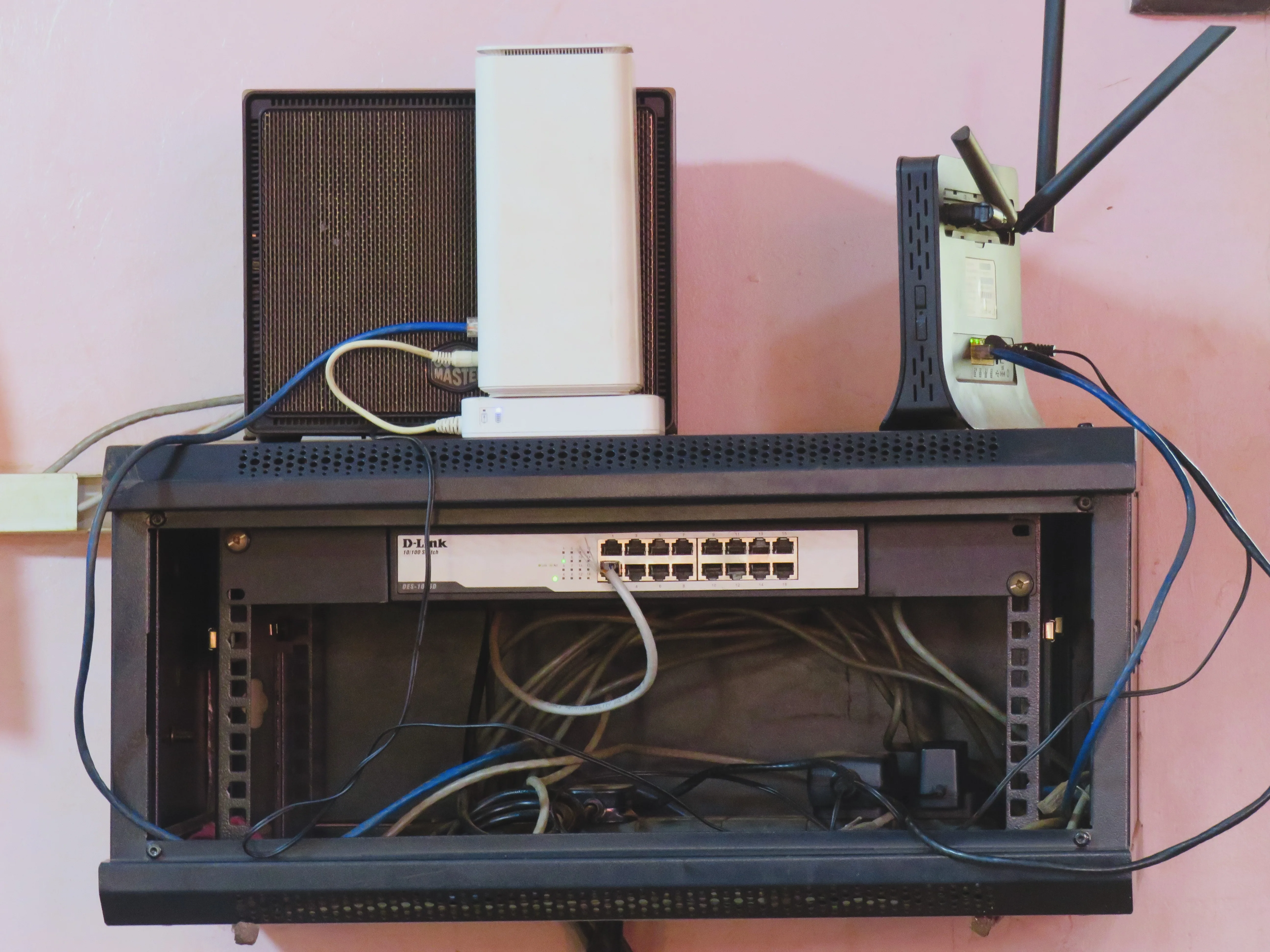 Wall-mounted network rack holding an Ethernet switch, routers and connected cables