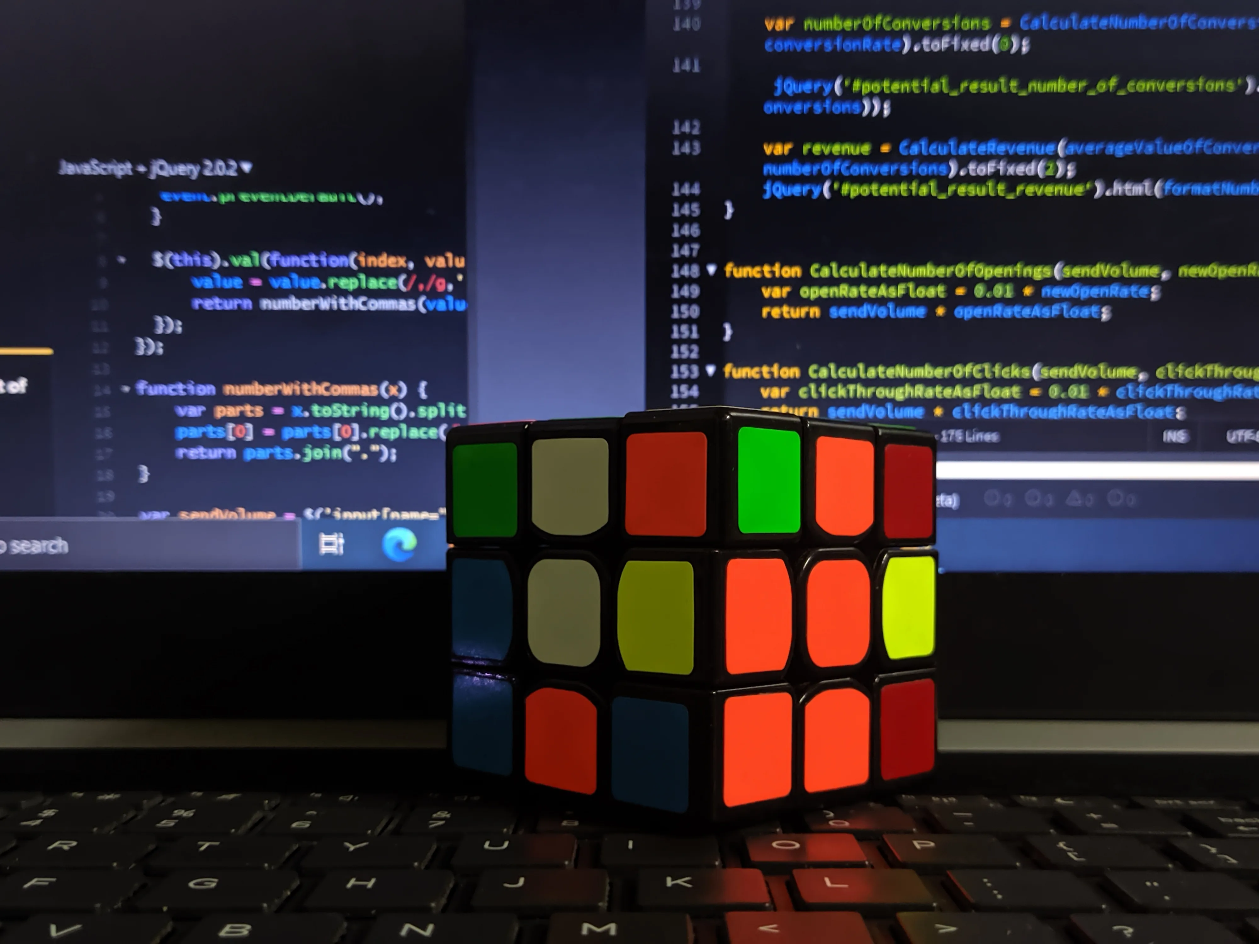 Multicolored puzzle cube in front of a laptop displaying code