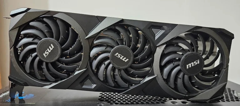 Three black cooling fans on an MSI GeForce RTX 3070 VENTUS 3X OC graphics card resting on a computer case