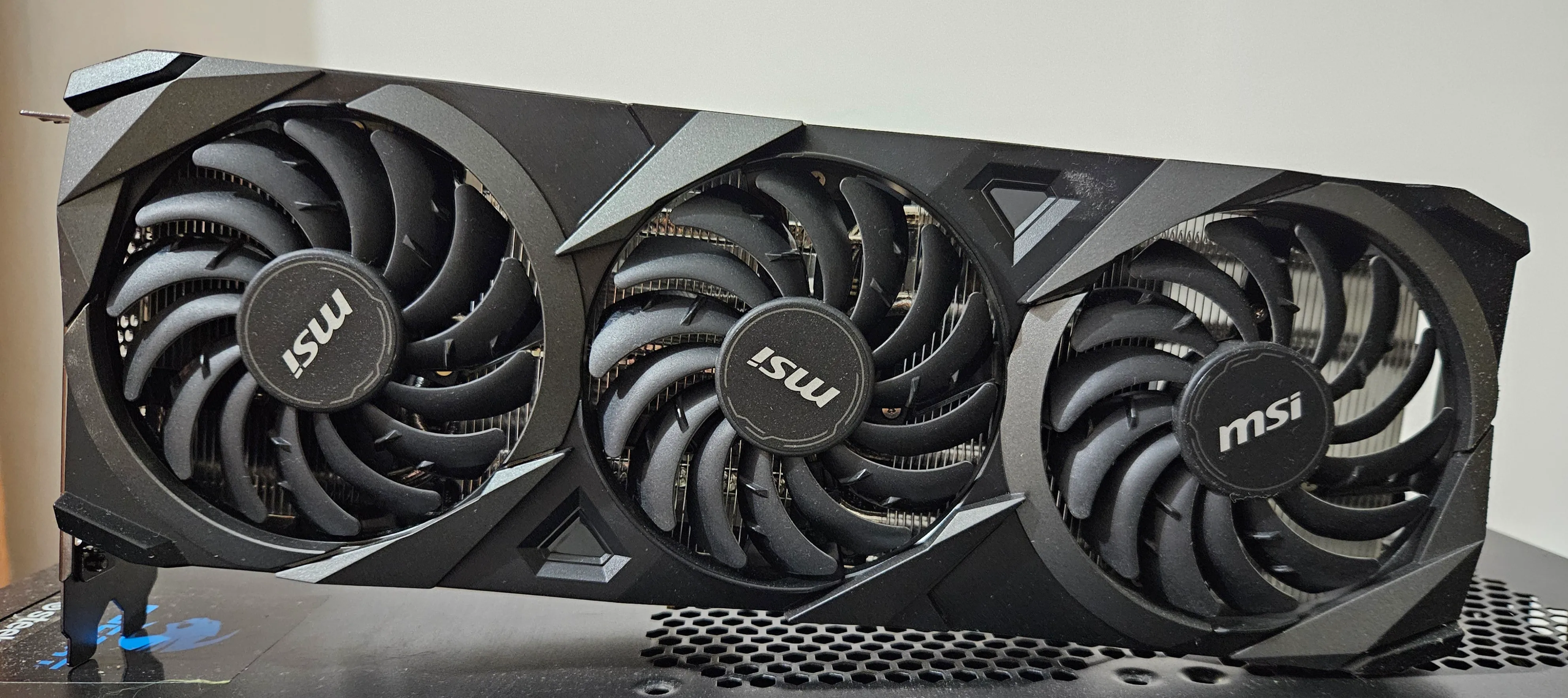 Three black cooling fans on an MSI GeForce RTX 3070 VENTUS 3X OC graphics card resting on a computer case