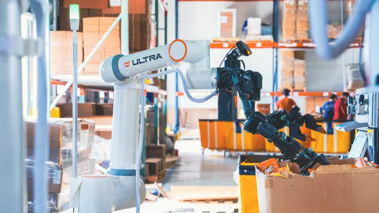 An Ultra OP1 robot beside a box of packaged items in a warehouse