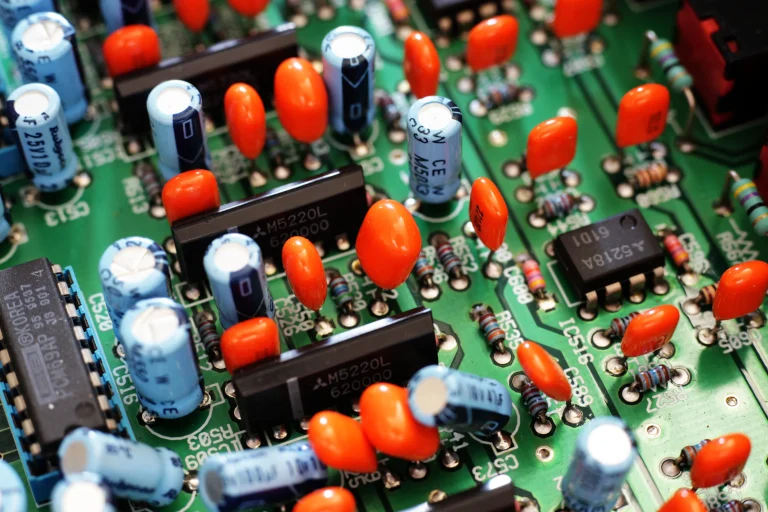 Orange and blue electronic components and black chips on a green circuit board