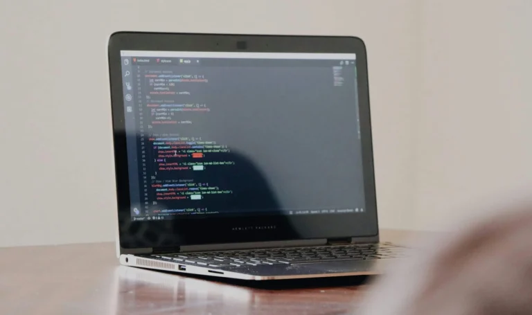 Laptop displaying JavaScript code in a code editor on a wooden desk