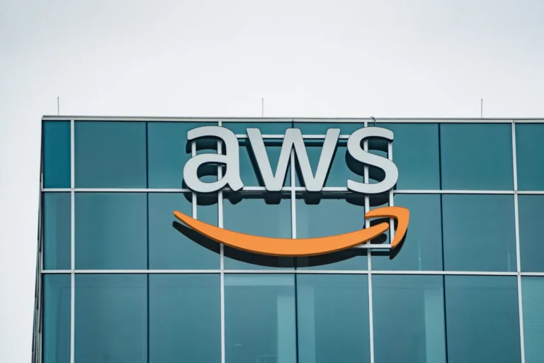 White AWS letters and an orange smile logo mounted on a glass office facade beneath a pale sky