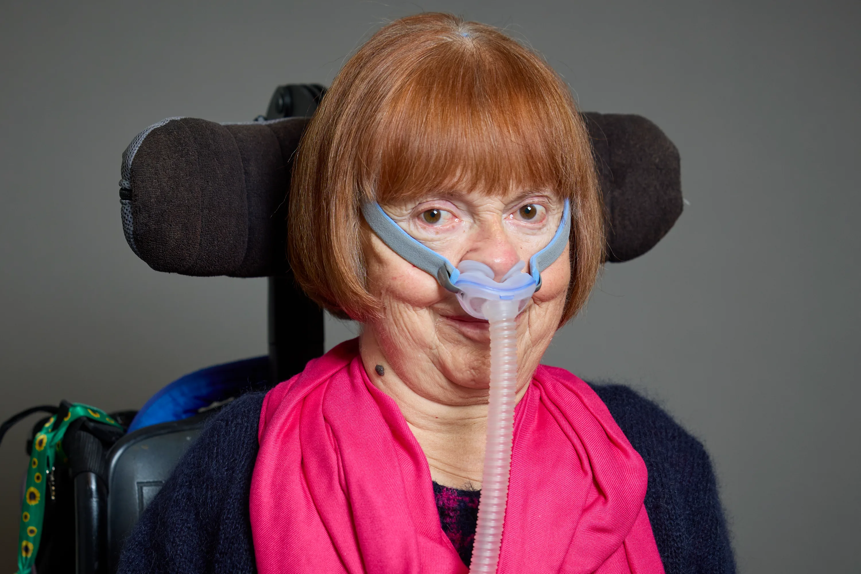 Official portrait of Baroness Campbell of Surbiton wearing a pink scarf and seated in her wheelchair.