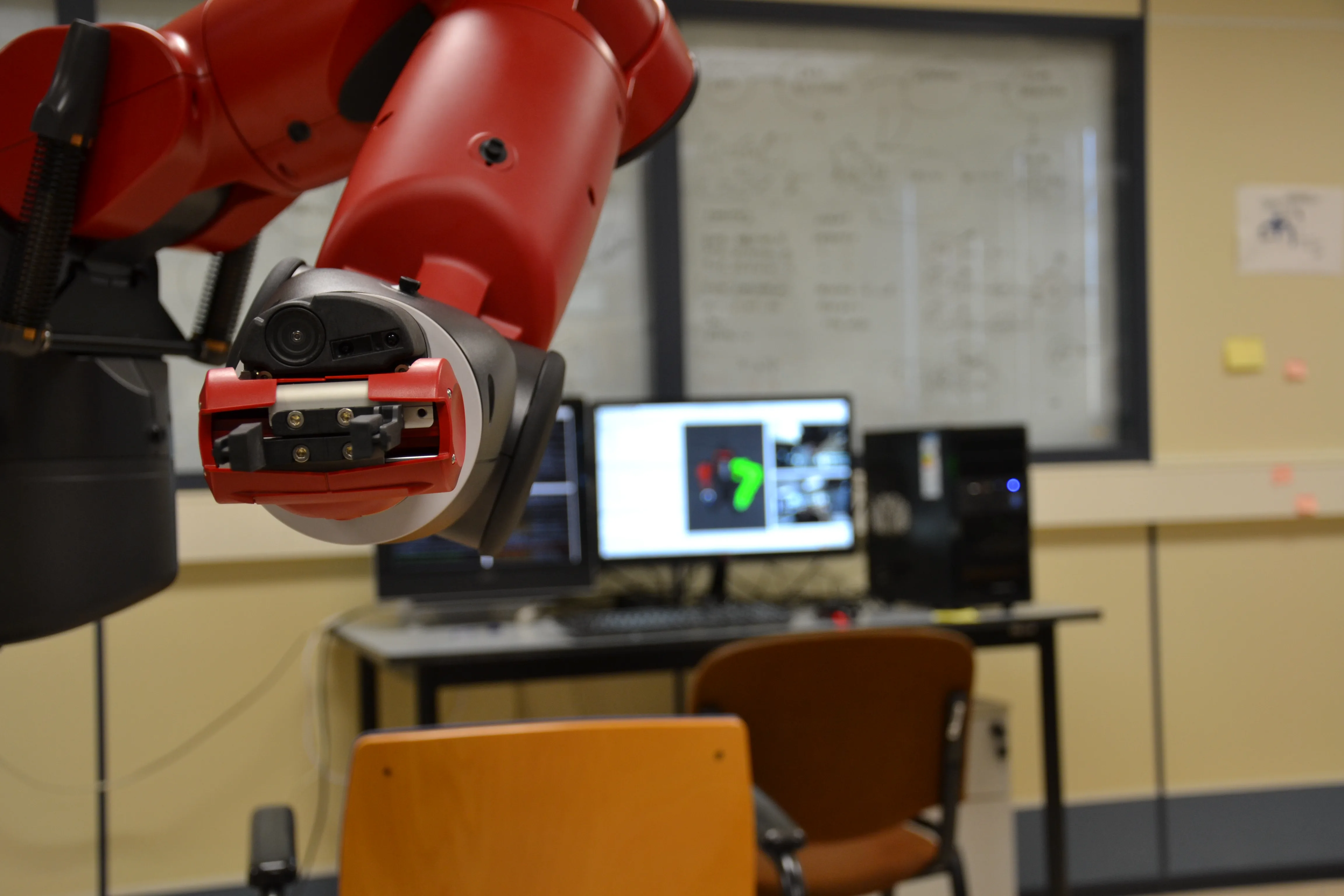 Red Baxter robot arm and gripper in the foreground of a robotics laboratory