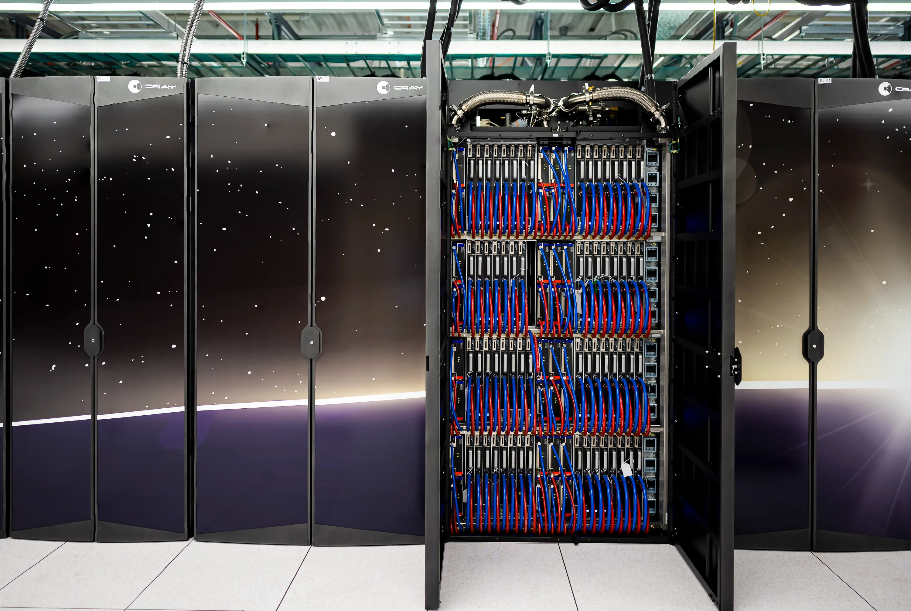 An open computing cabinet with rows of modules and red and blue connections beside closed black cabinets.