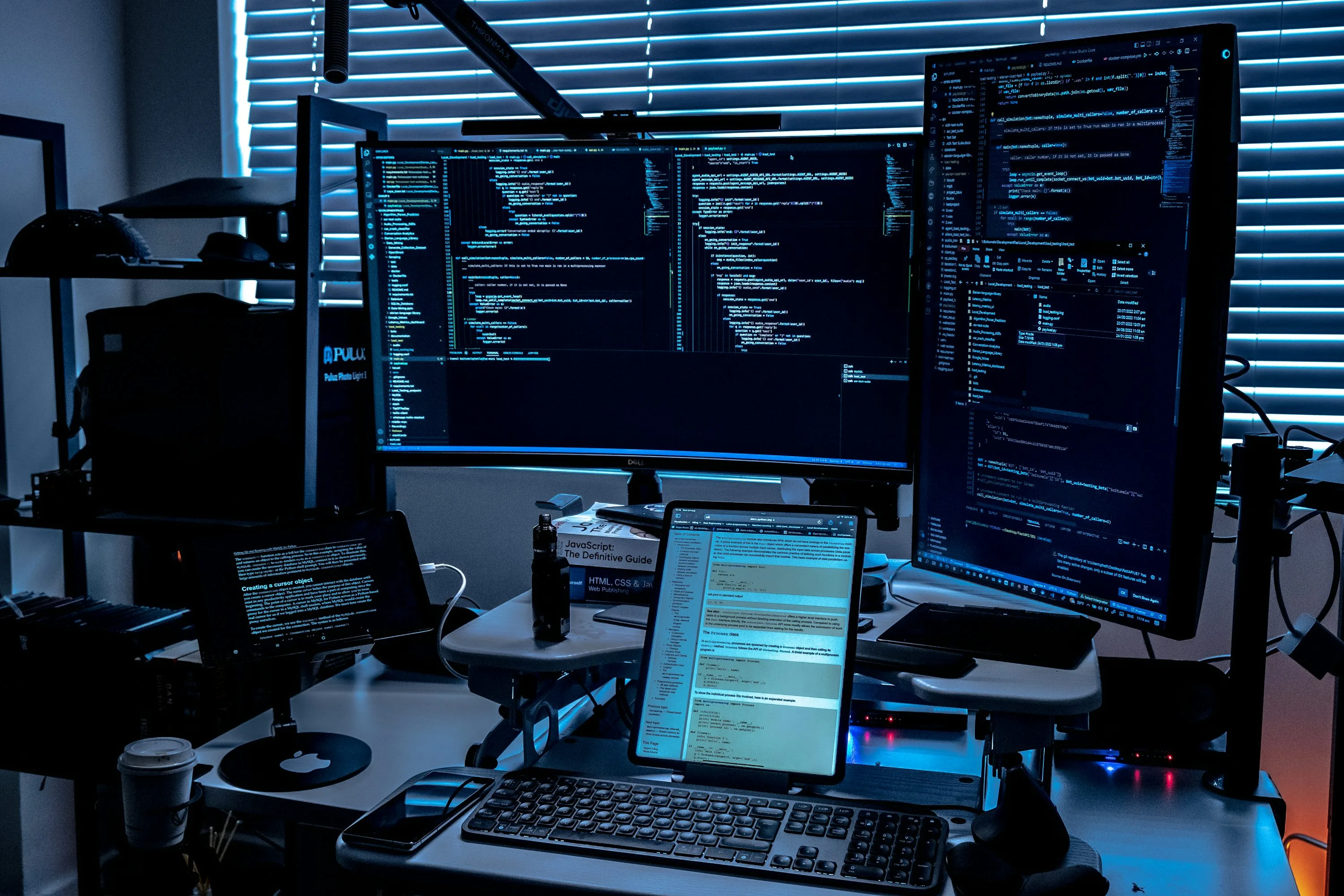 Two monitors and two tablets display code and programming documentation at a desk