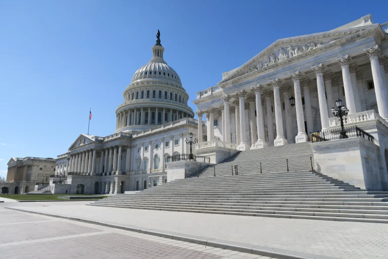The white dome, columns and broad entrance steps of the United States Capitol under a clear blue sky