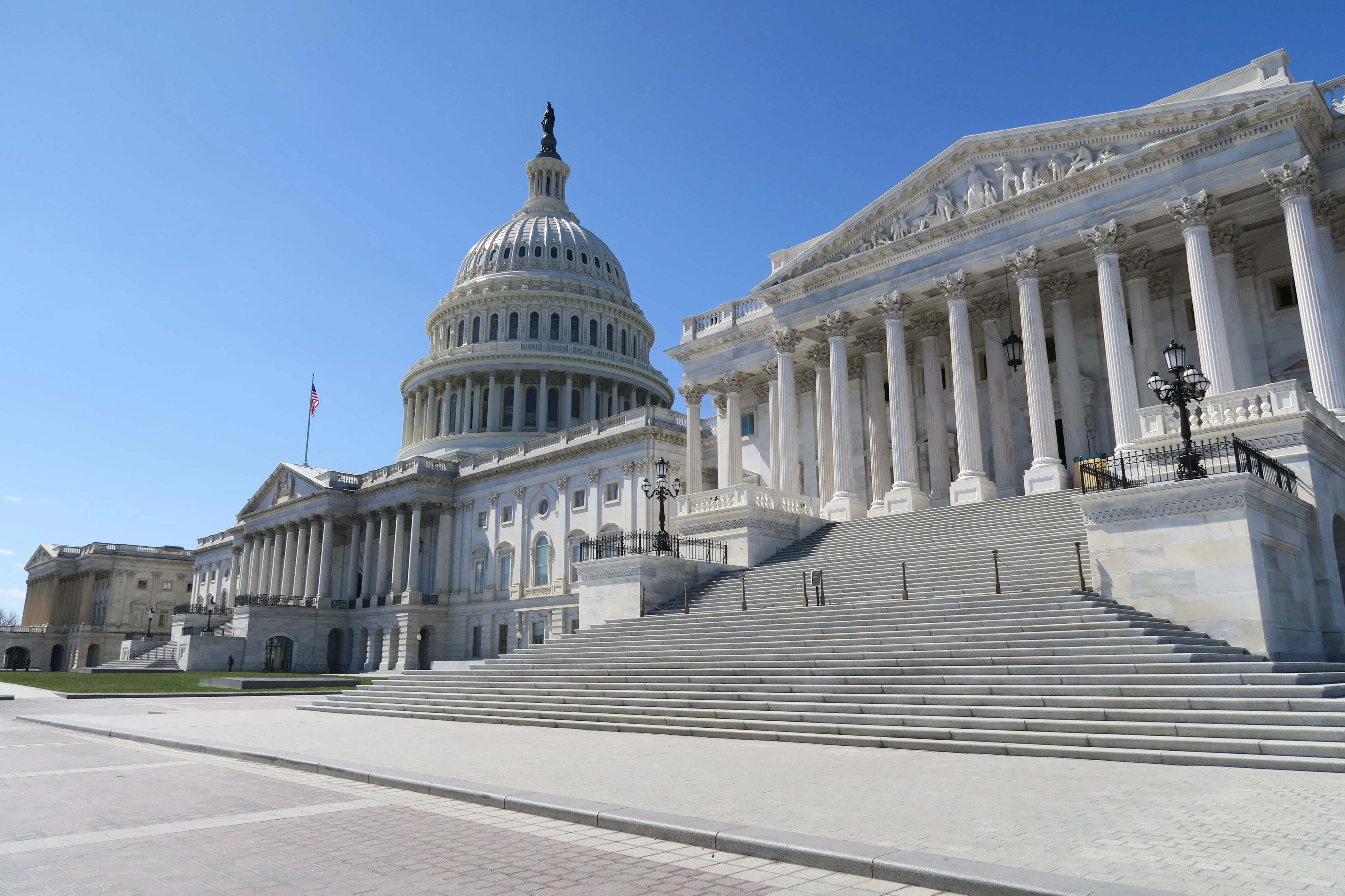The white dome, columns and broad entrance steps of the United States Capitol under a clear blue sky