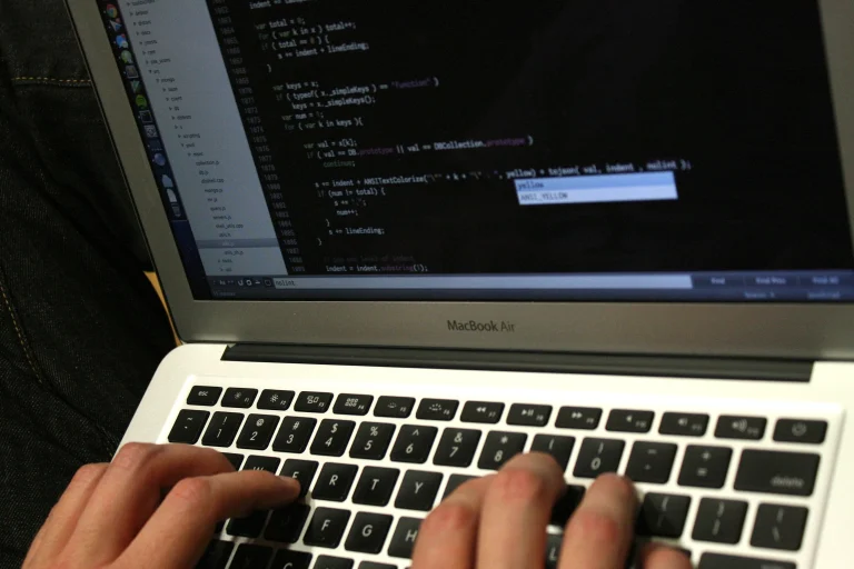 Hands type on a silver MacBook Air with source code visible on its dark screen