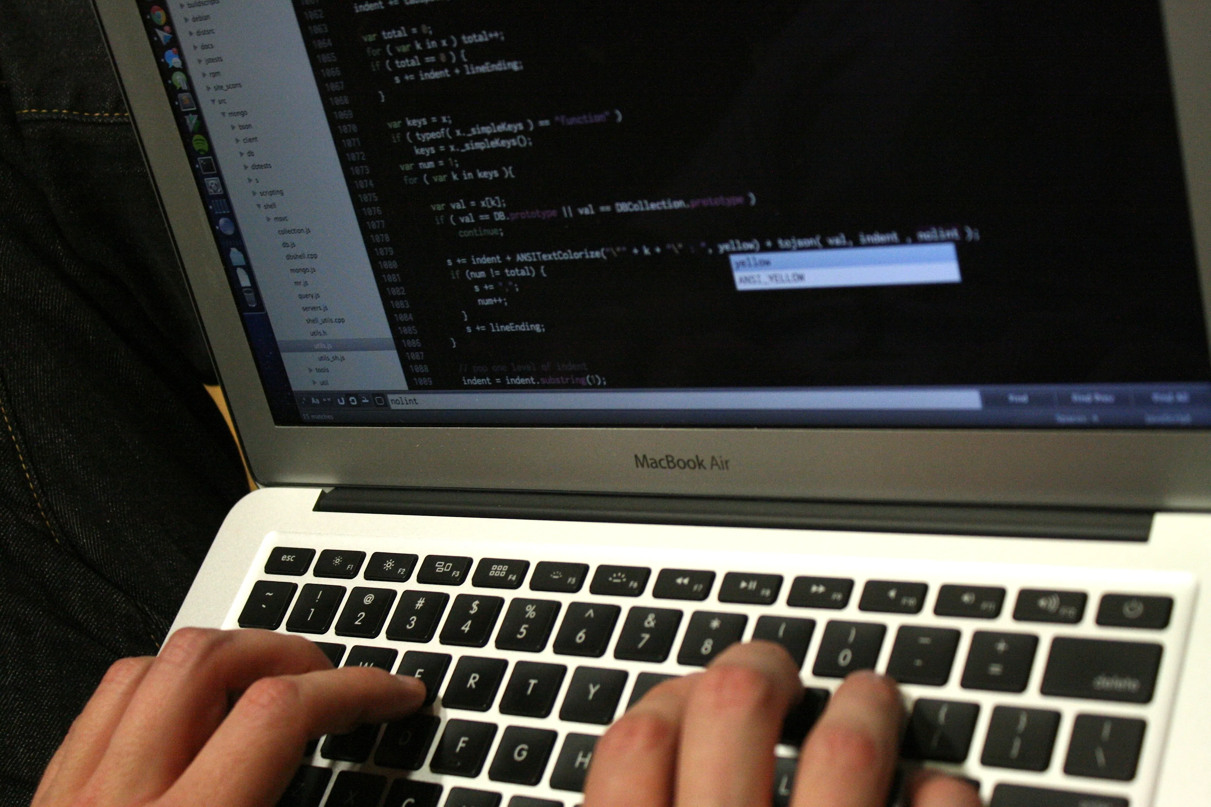 Hands type on a silver MacBook Air with source code visible on its dark screen