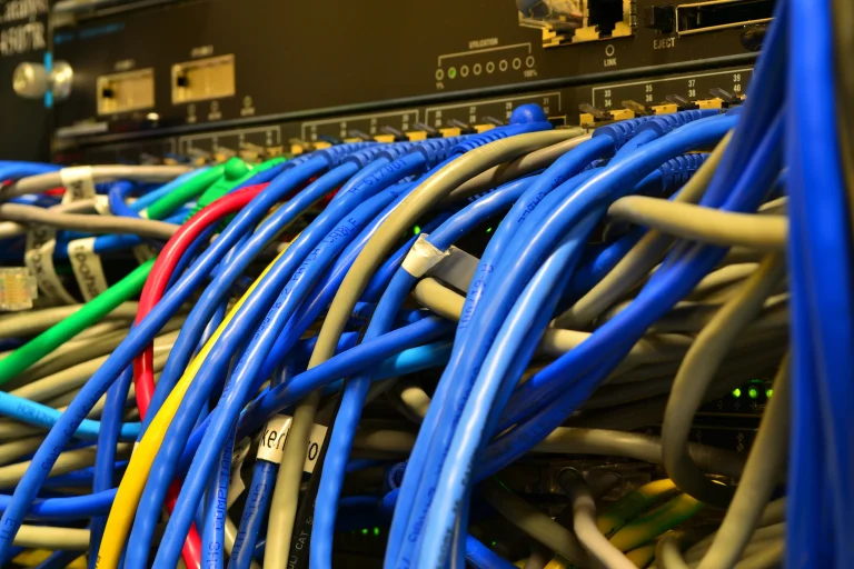 Blue, gray, red and green Ethernet cables connect to a black network switch with rows of ports and green indicator lights.