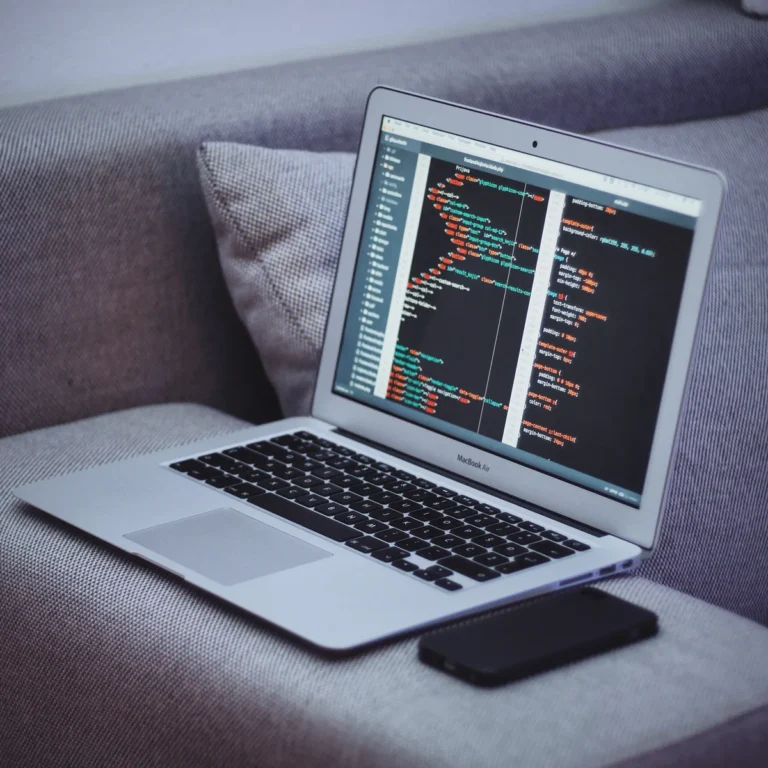 Laptop displaying source code on a gray sofa with a phone beside it