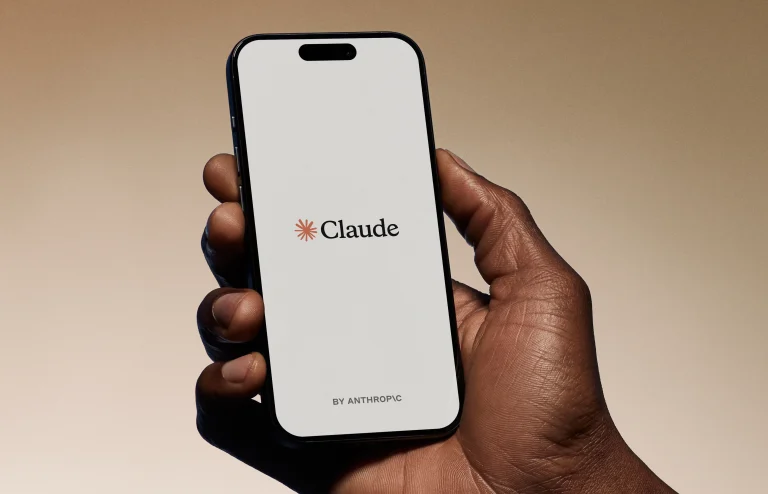 A hand holding a smartphone with Claude on the screen