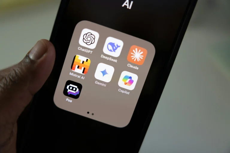 A hand holding a smartphone with the Claude app beside other AI apps