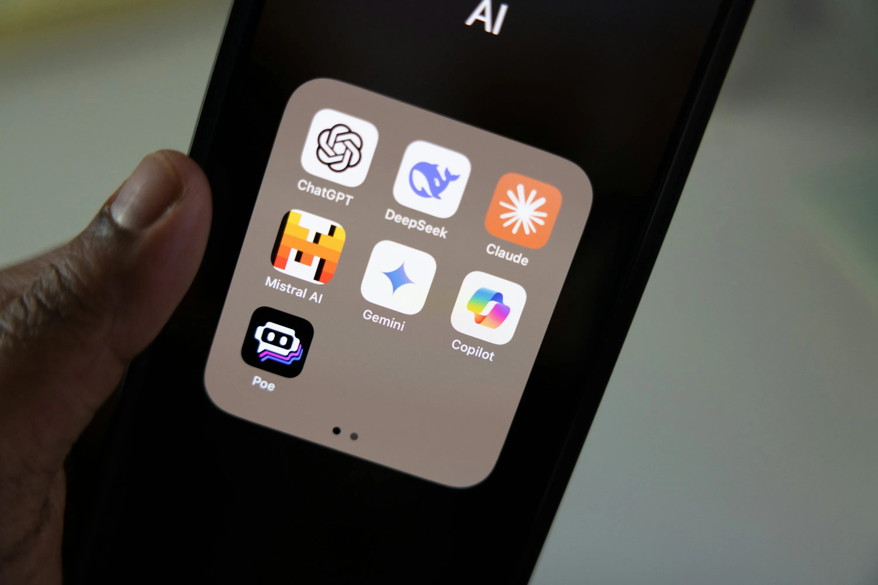 A hand holding a smartphone with the Claude app beside other AI apps