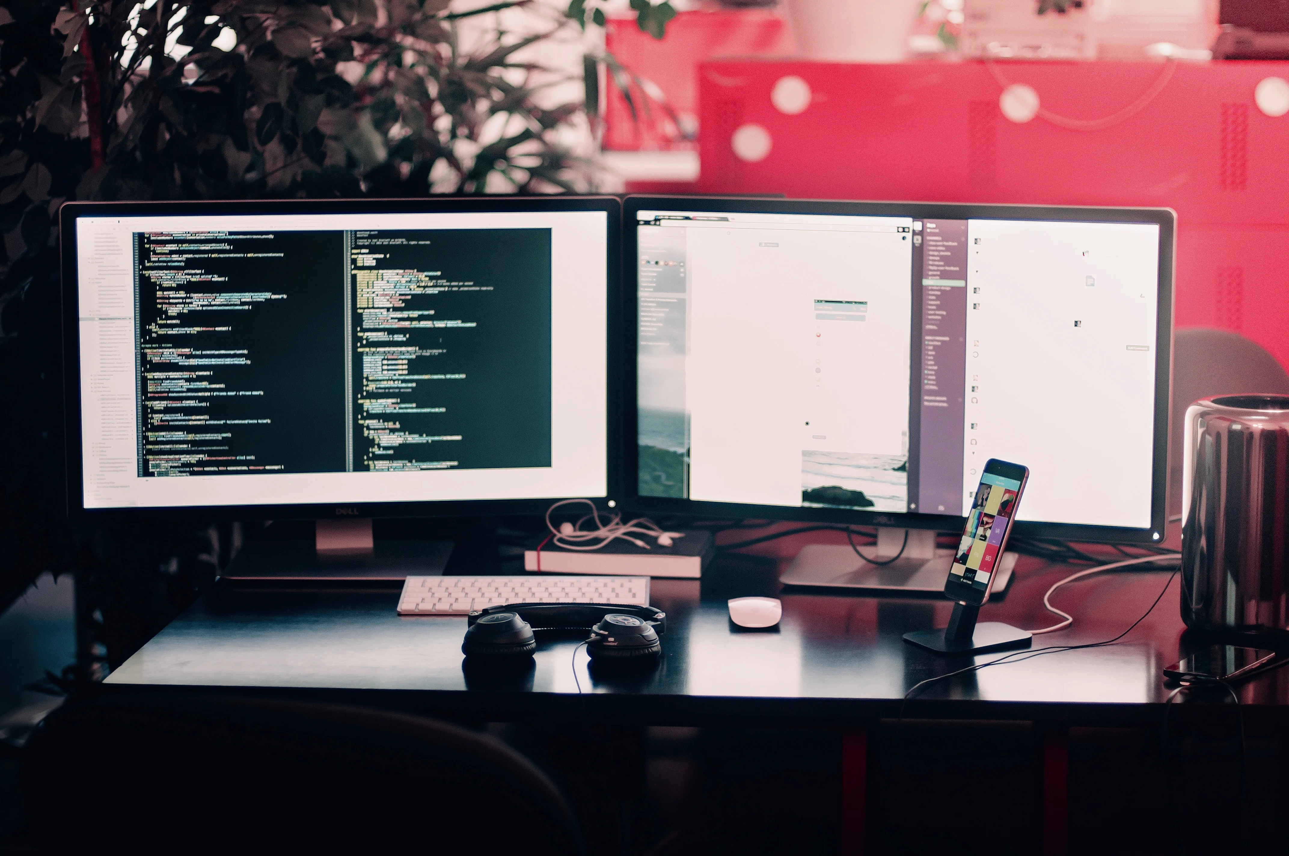 Two monitors on a desk with code on the left screen, a keyboard and headphones