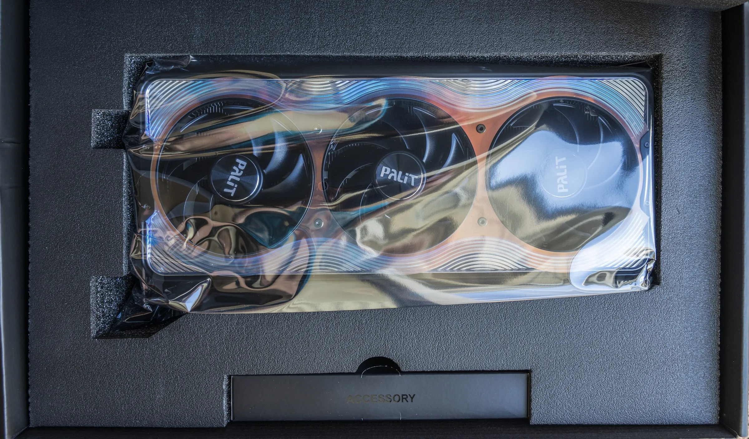 A Palit GeForce RTX 5090 GameRock graphics card with three cooling fans inside protective packaging