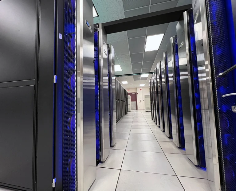 An aisle between tall server cabinets with blue lights at NASA’s Cabeus supercomputer