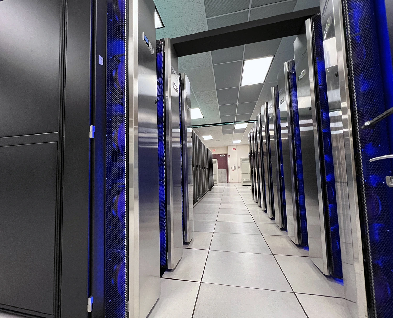 An aisle between tall server cabinets with blue lights at NASA’s Cabeus supercomputer