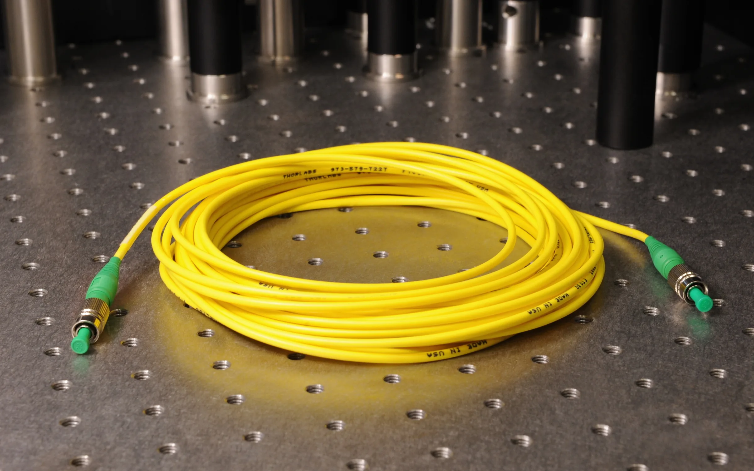 A yellow optical fiber patch cable with FC connectors on an optical table