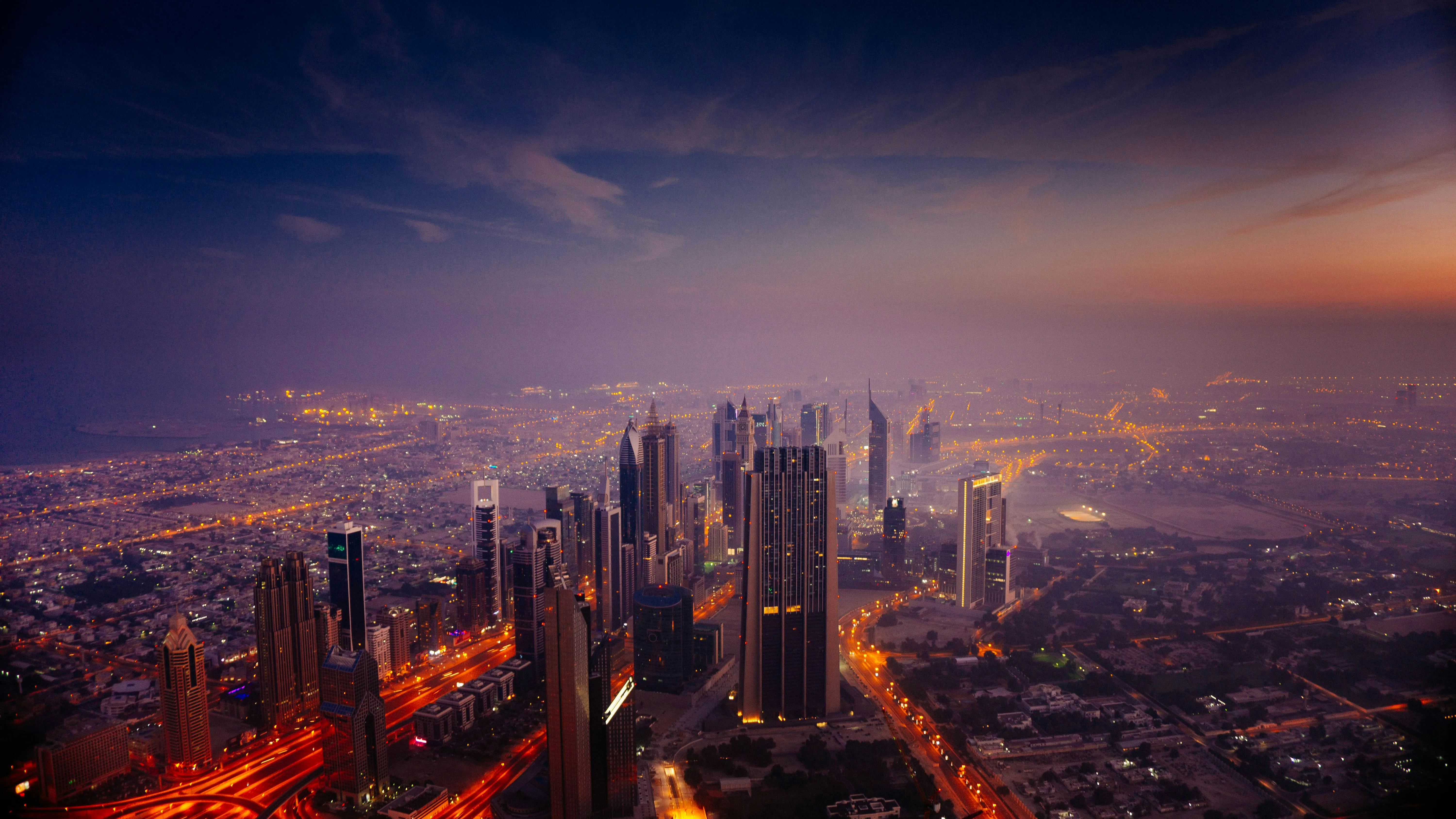 Dubai skyscrapers and illuminated roads beneath a hazy purple and orange sky