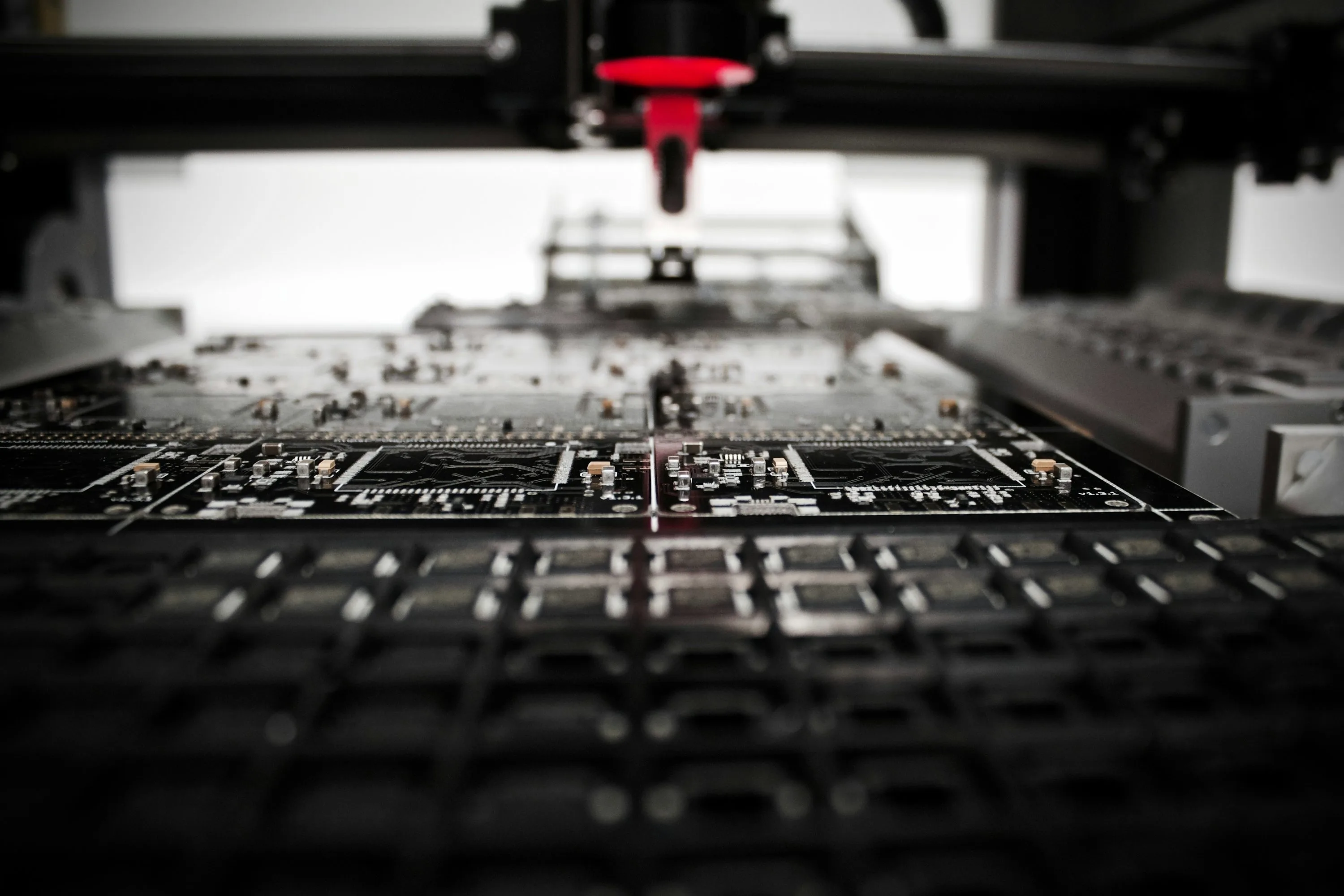 A red machine head sits above rows of black printed circuit boards in an electronics production machine