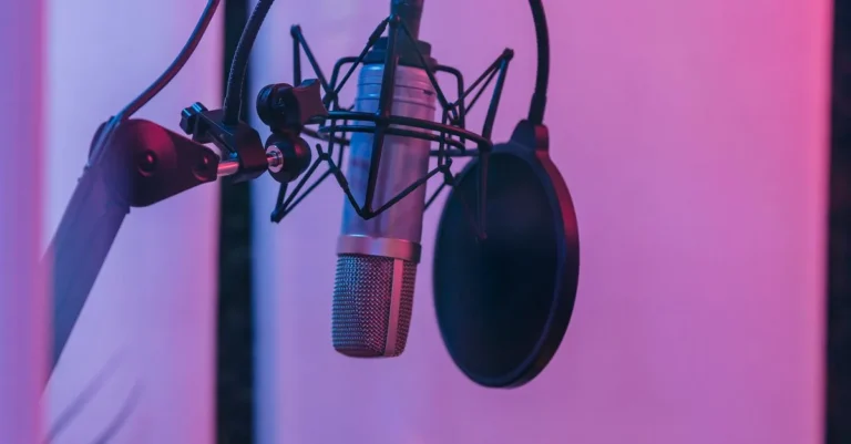 A silver studio microphone and black pop filter under purple lighting