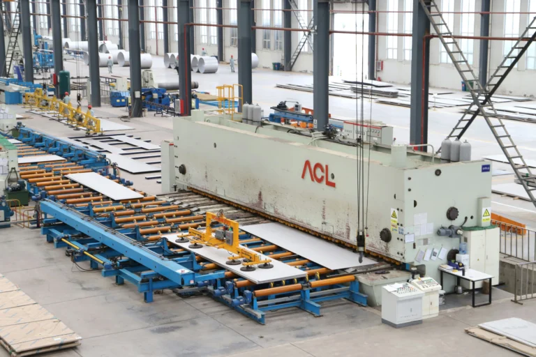 Large metalworking machine and roller conveyors carry metal sheets across a bright factory floor