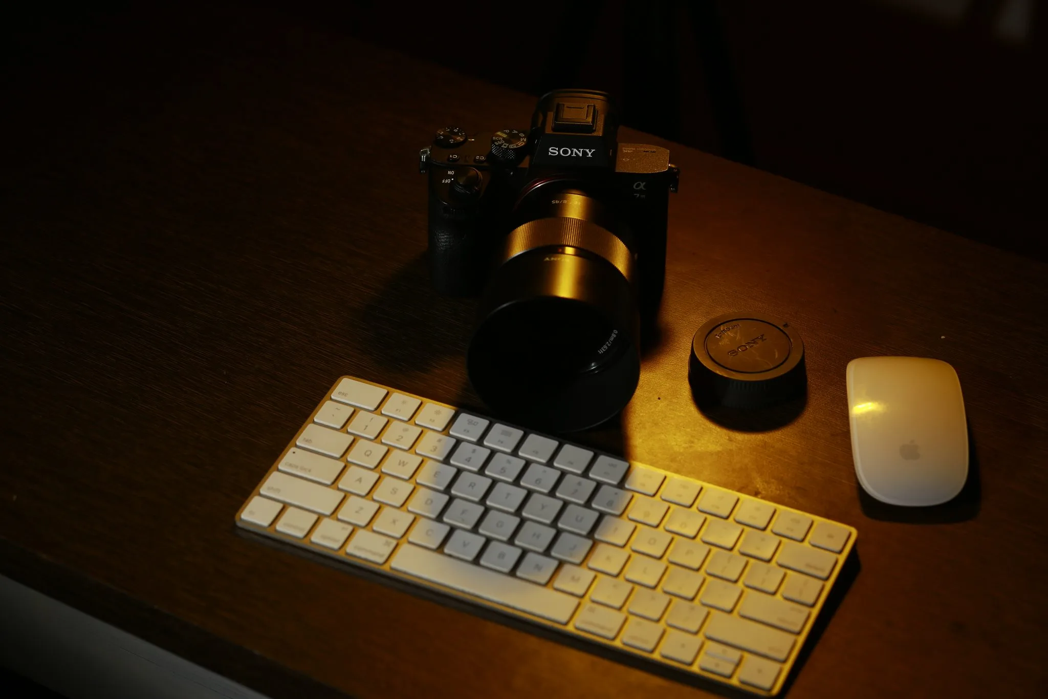 Camera and lens on a wooden desk beside a white keyboard and mouse