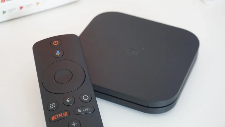 Black Xiaomi Mi Box S media player and remote control on a white surface.
