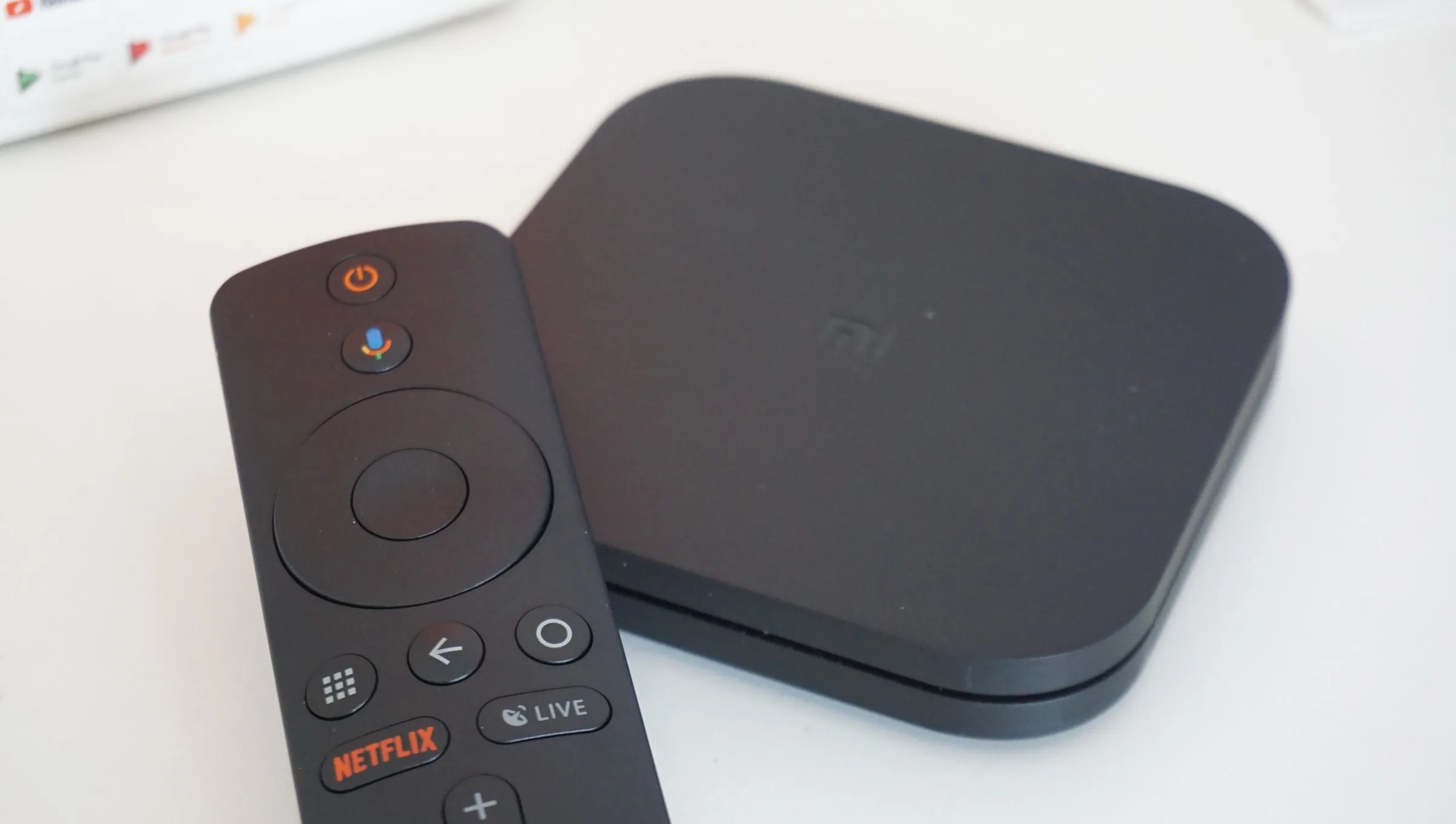 Black Xiaomi Mi Box S media player and remote control on a white surface.