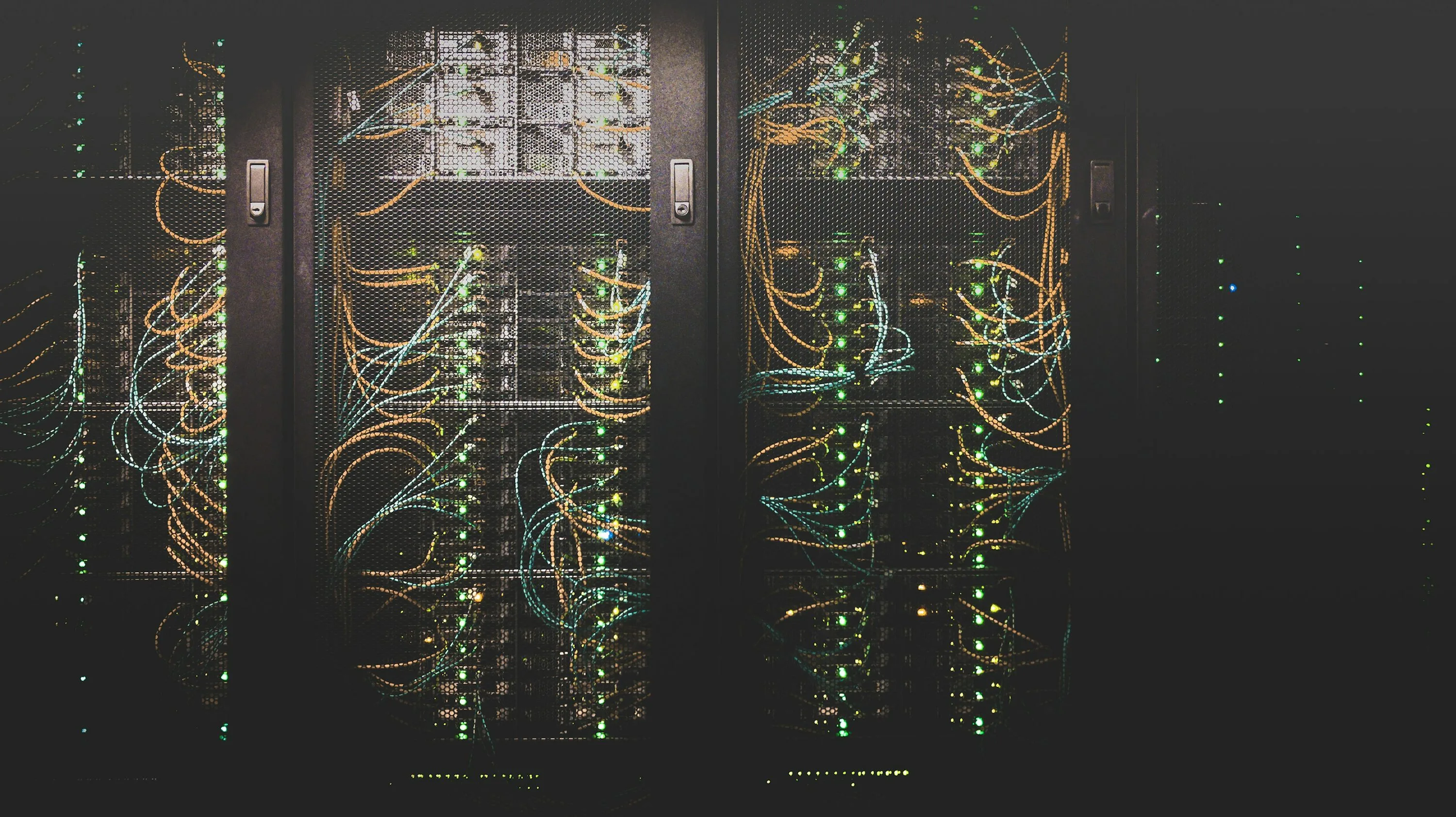Orange and blue network cables and green lights behind black mesh doors in server racks
