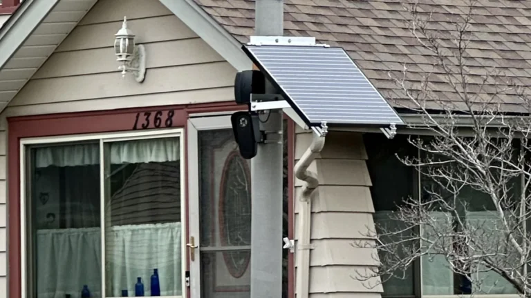 A black Flock Safety camera and a solar panel attached to a metal pole in front of a house