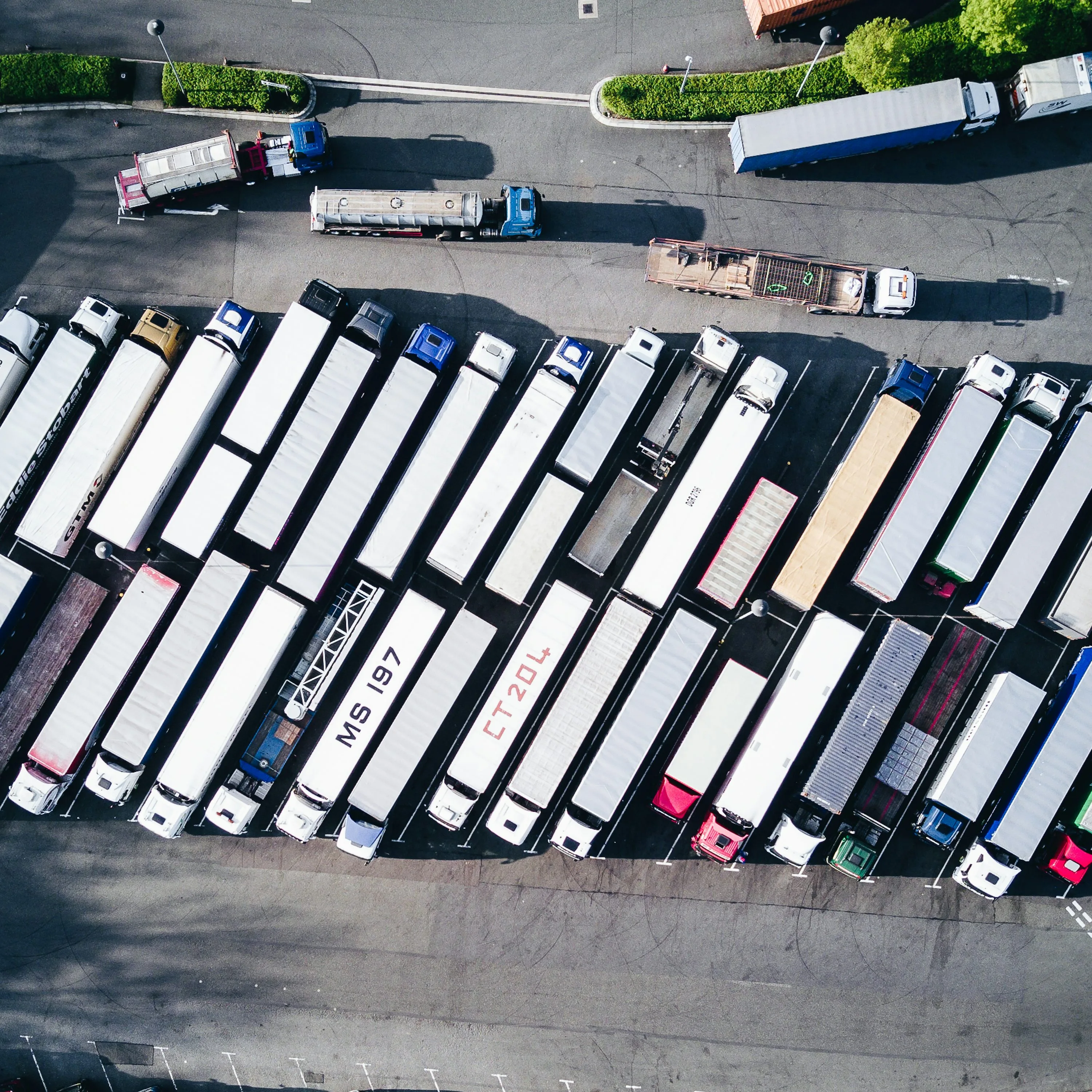An overhead view shows rows of freight trucks parked in a lot with several trucks in the access lane