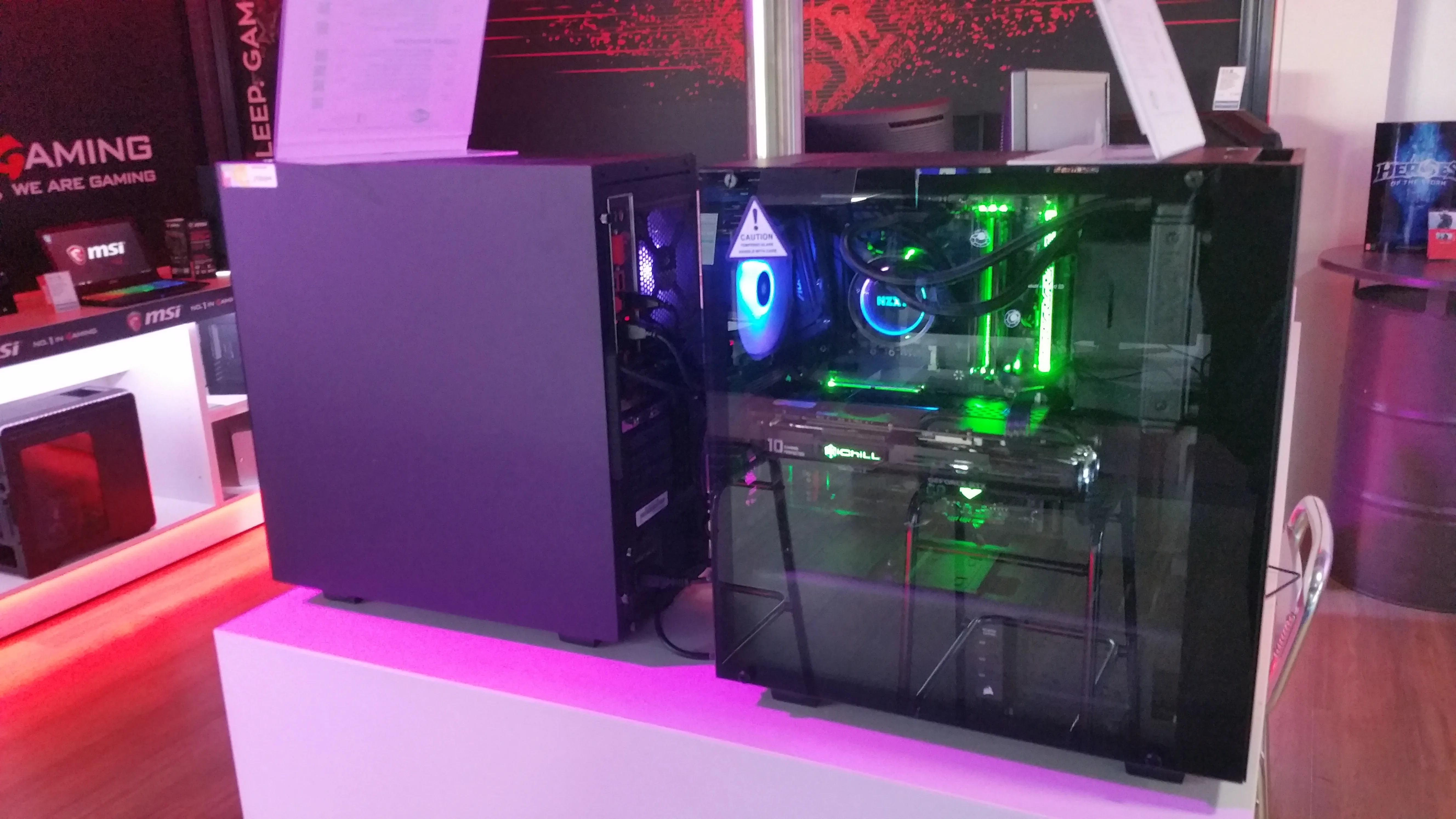 A gaming desktop with a glass side panel shows illuminated cooling fans and components on a computer shop display