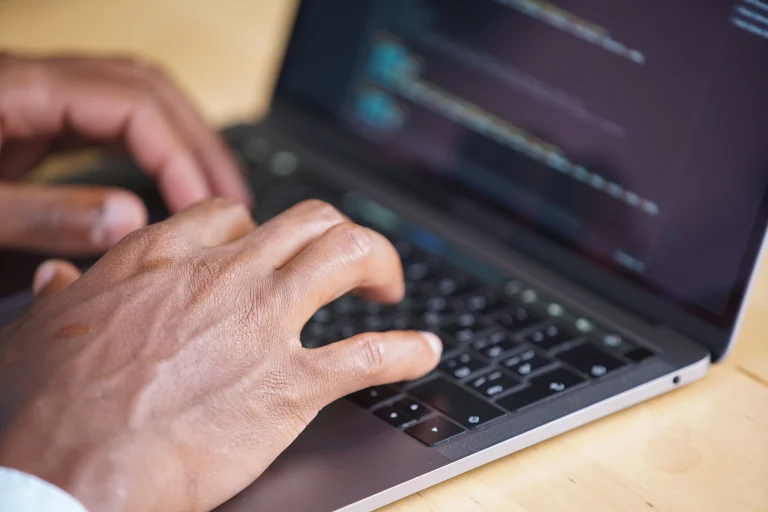 Hands typing on a laptop with a softly focused programming screen