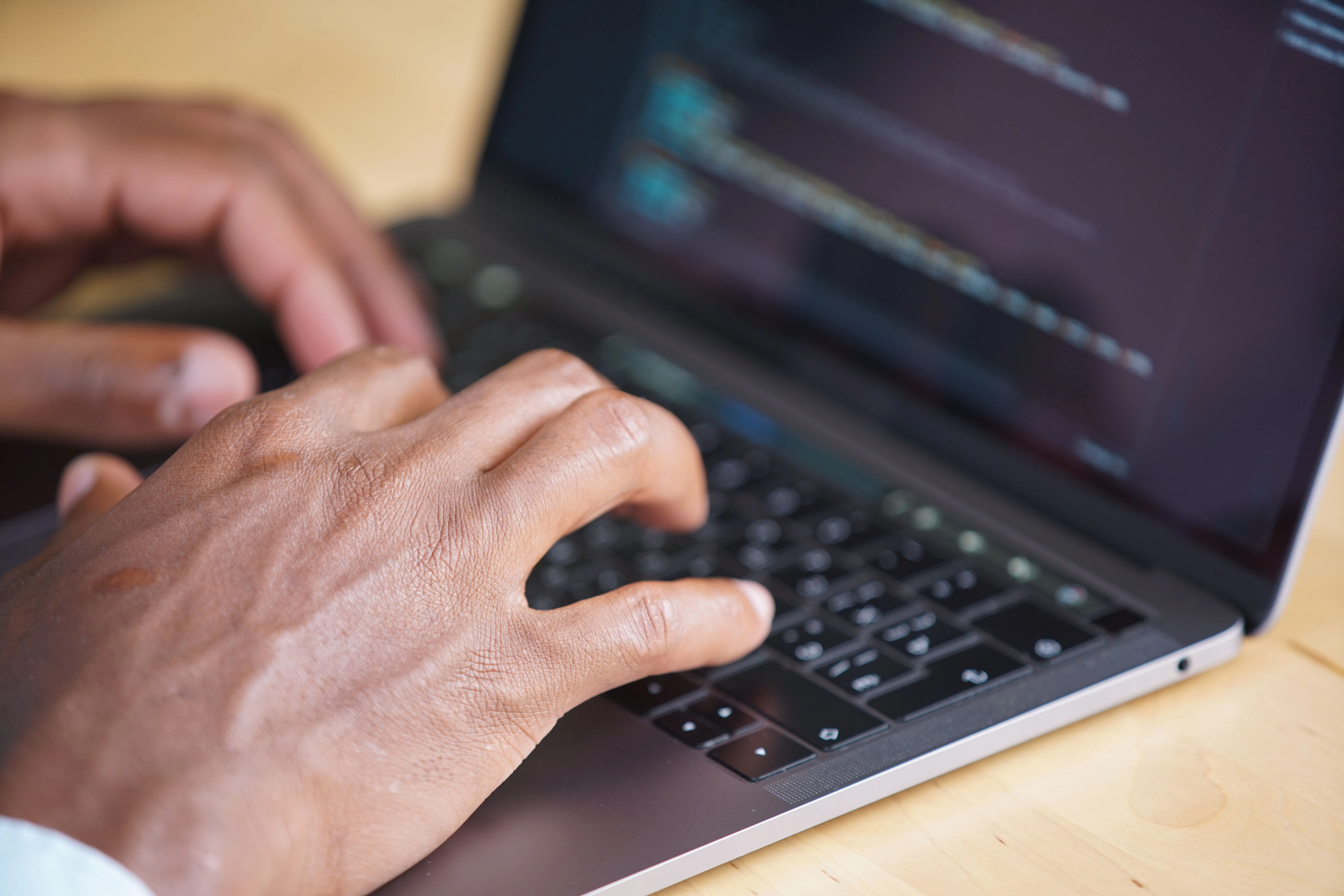 Hands typing on a laptop with a softly focused programming screen