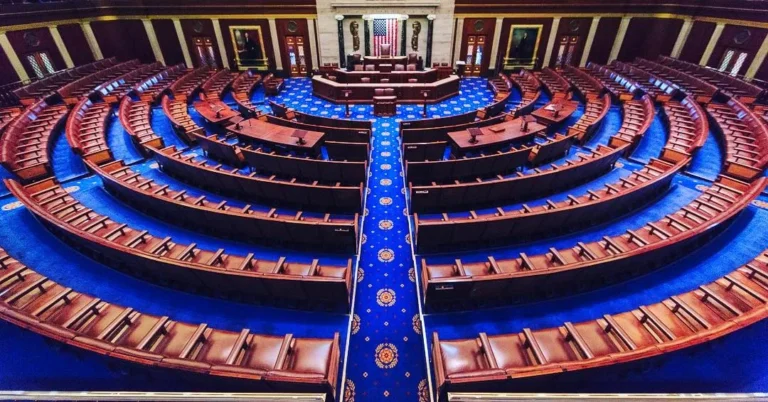 Empty House chamber with curved rows of seats and blue carpeting