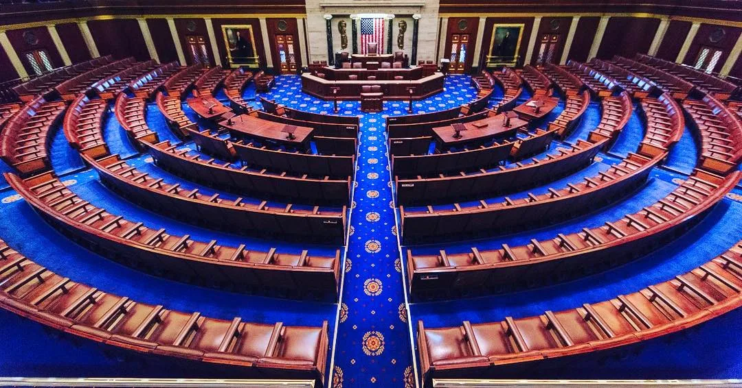 Empty House chamber with curved rows of seats and blue carpeting