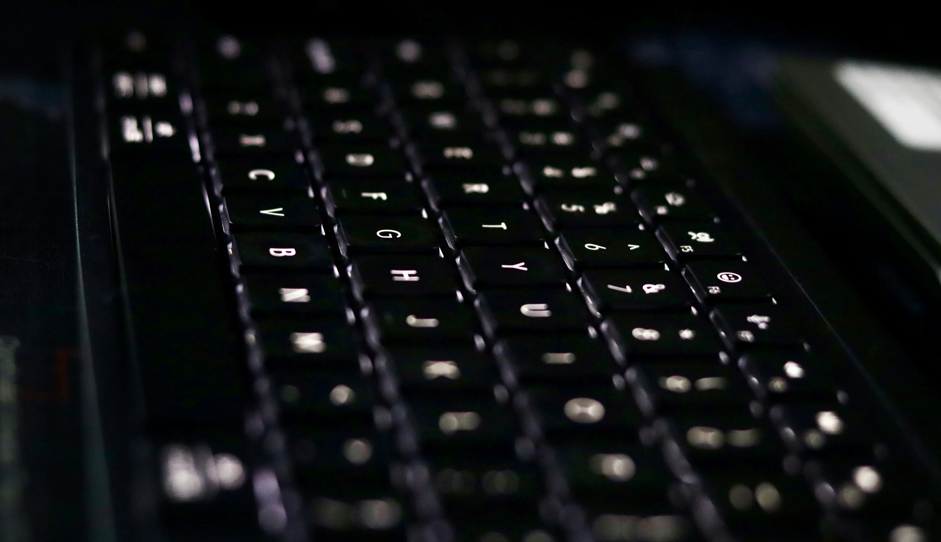 Close view of black computer keys with white backlighting and shallow depth of field