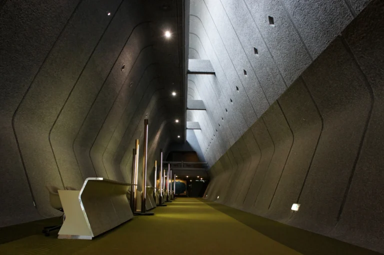 Tall angular concrete walls and a skylight above a green carpeted corridor inside Kyoto International Conference Center