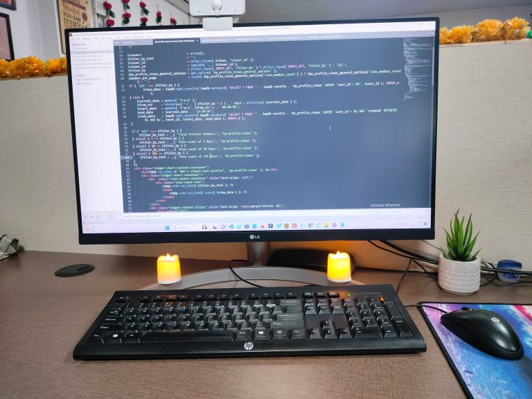 Desktop monitor displaying code above a keyboard beside candles and a small plant