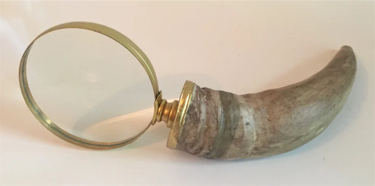 A round magnifying glass with a brass rim and curved textured handle rests on a pale surface