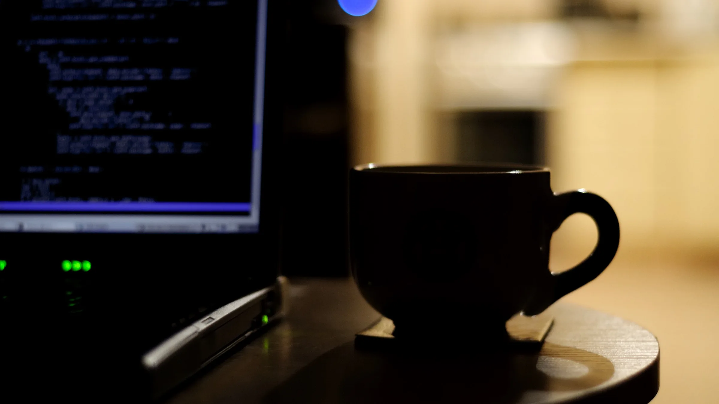 A laptop displaying softly focused source code beside a dark coffee cup on a wooden table