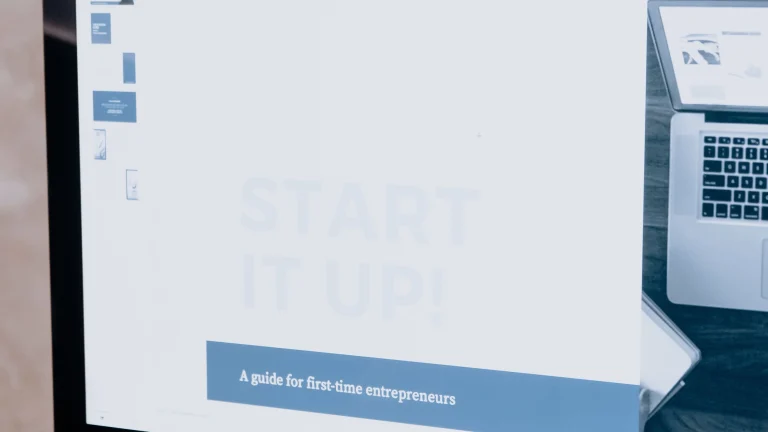 A desktop monitor displays presentation slides with a laptop photograph and a guide for entrepreneurs