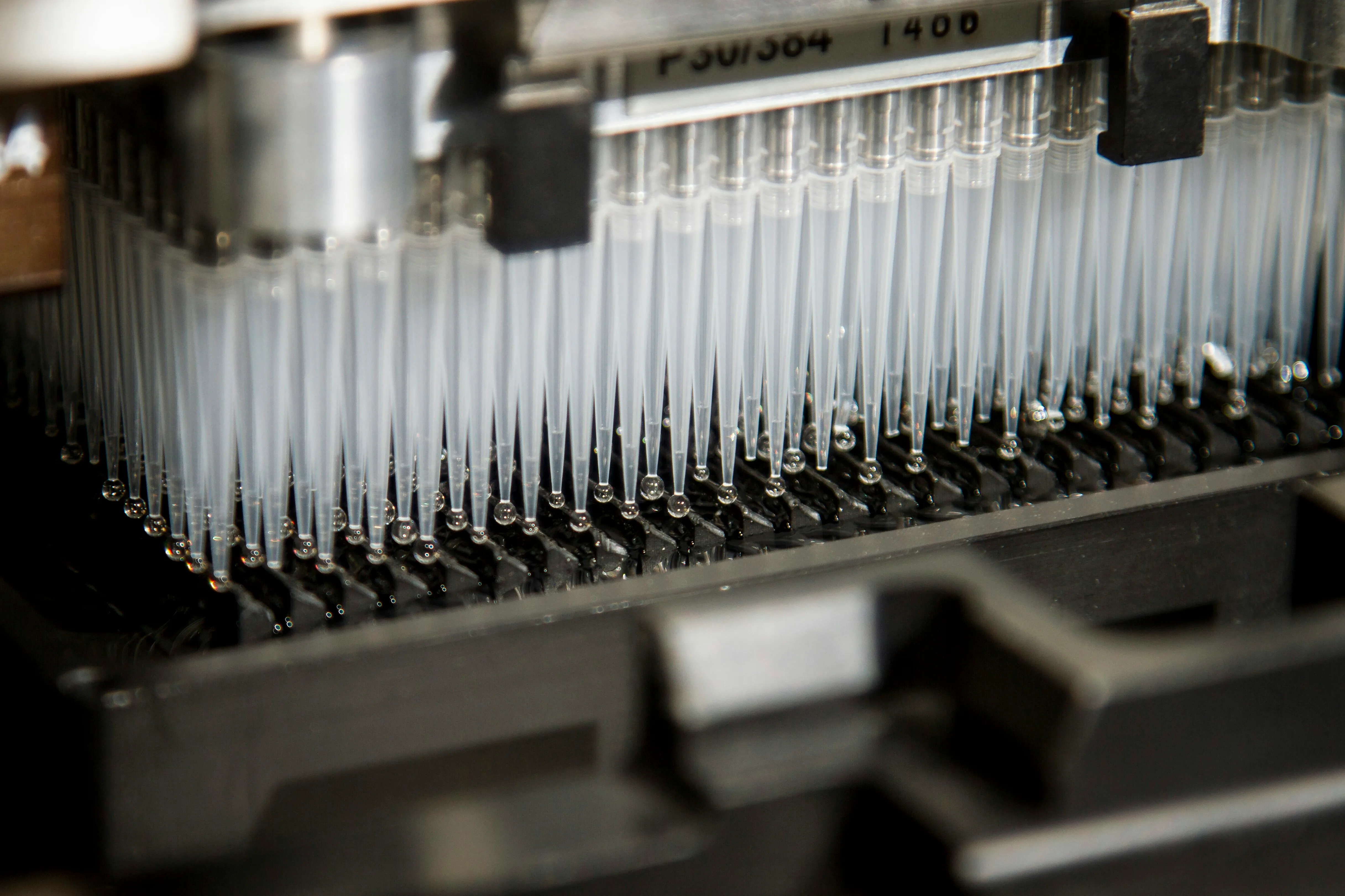 Rows of transparent pipette tips dispensing droplets inside automated laboratory equipment