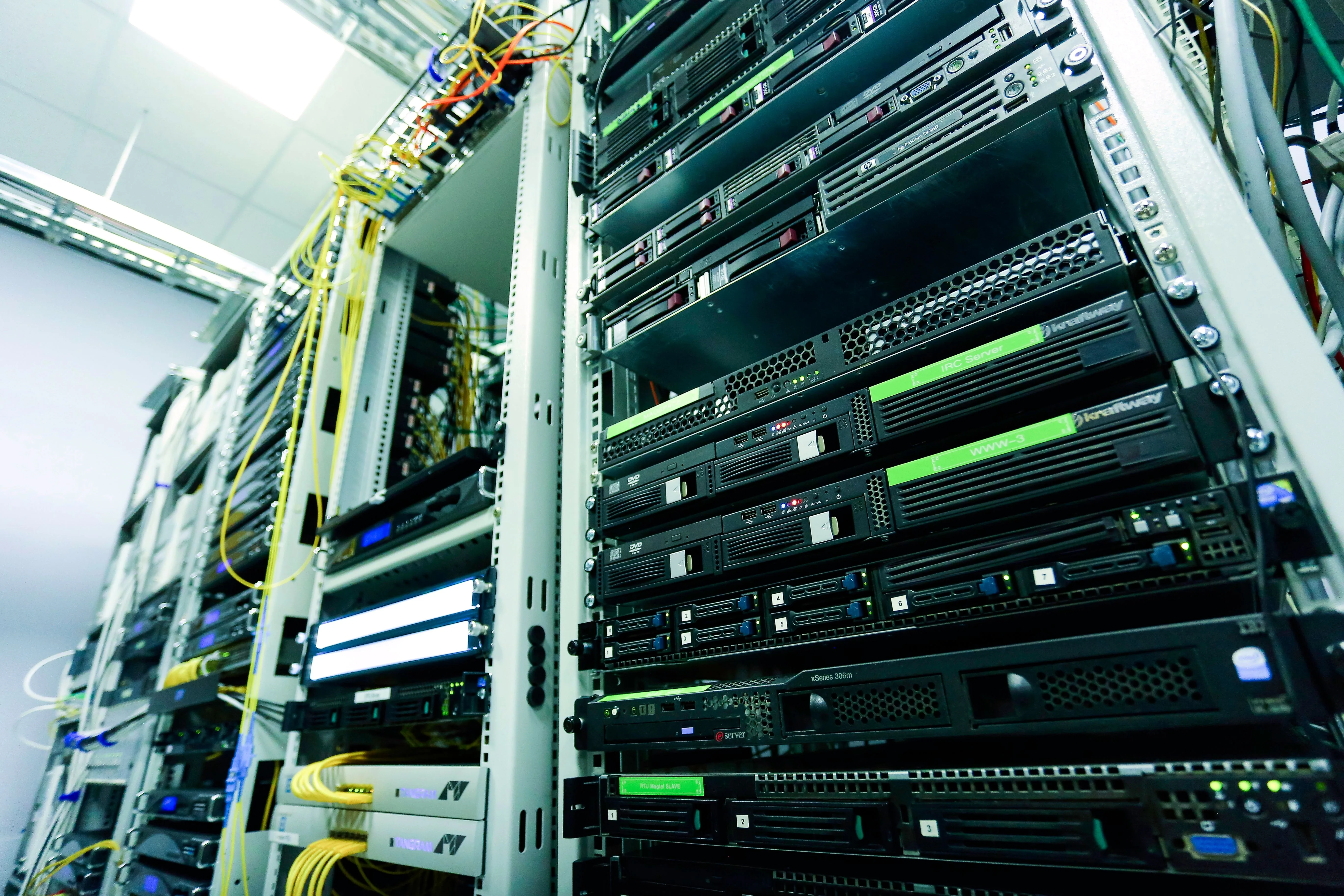 Black servers fill equipment racks with yellow and green network cables beside them